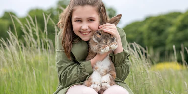 A young girl holding a rabbit in a field.